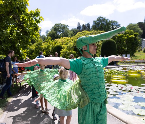 Ein Tänzer im Krokodilskostüm übt mit Kindern in der Wilhelma den Krokodilstanz ein