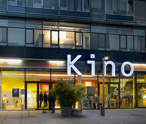 Ein Kino·gebäude ist zu sehen. Es ist hell beleuchtet. In großen Buchstaben steht Kino an der Wand.